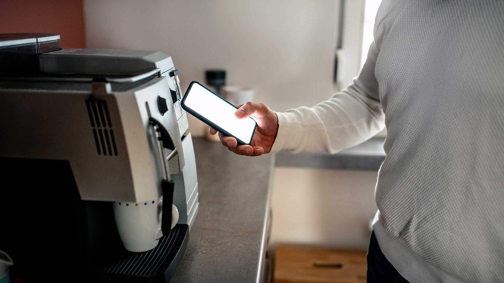 A person uses their smart phone app to control the coffee machine to make a coffee.